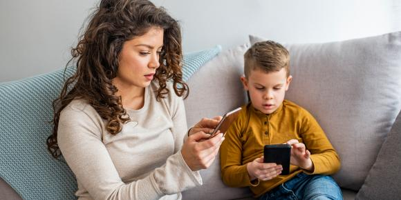 Mutter und Kind am Handy, sitzen zusammen auf einem Sofa.